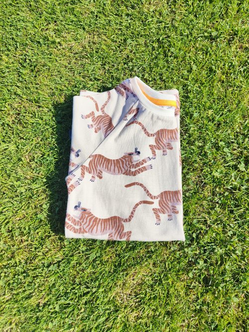 T-shirt plié manches courtes raglan tiger tales avec un motif tigre japonisant couleur ocre sur fond beige. On aperçoit la bande de propreté qui vient donner une finition impeccable au t-shirt
